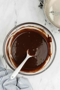 melted chocolate in a glass bowl with a spoon on the side next to two silver pans