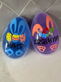 two plastic easter eggs with cartoon characters painted on them, one is blue and the other is purple