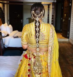 the back of a woman's head wearing a yellow lehenga and jewelry