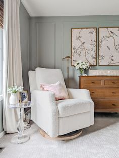 a white rocking chair sitting in a living room next to a dresser