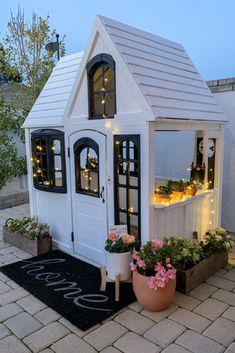 a small white house with potted plants and lights