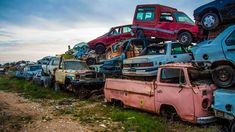 a bunch of old cars stacked on top of each other in a junk yard with grass and dirt