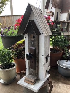 a bird house sitting on top of a wooden table next to potted plants and flowers