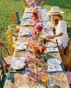 a long wooden table with plates and flowers on it is set for an outdoor dinner