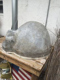 an old metal helmet sitting on top of a wooden table next to plants and other items