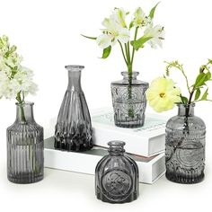 four glass vases with flowers in them sitting on a white book and some books