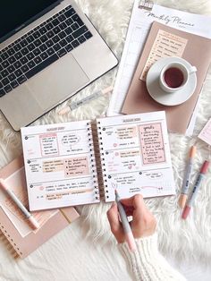 a person is writing in a planner next to a laptop and cup of coffee on a fluffy white blanket