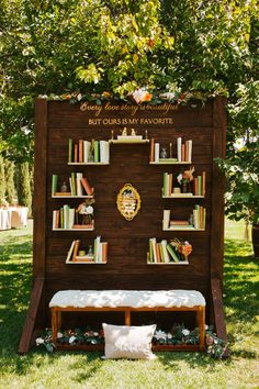 a wooden book shelf with books on it and a bench under the tree in front of it