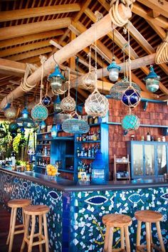 an outdoor bar with lots of hanging lights and decorations on the ceiling, along with wooden stools