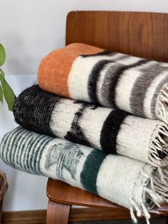 three different colored blankets sitting on top of a wooden chair next to a potted plant