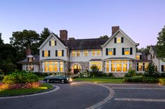 a car is parked in front of a large white house with green shuttered windows