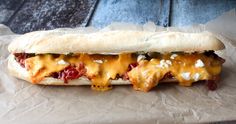 a sub sandwich with cheese and other toppings sitting on top of waxed paper