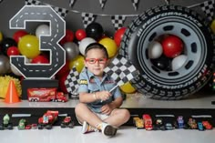 a young boy is sitting on the floor with his race car themed birthday party decorations