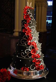 a three tiered wedding cake with red flowers on the bottom and silver trimmings