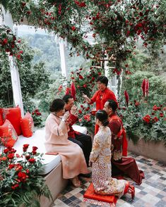 three women sitting on a bench talking to each other in front of red flowers and greenery