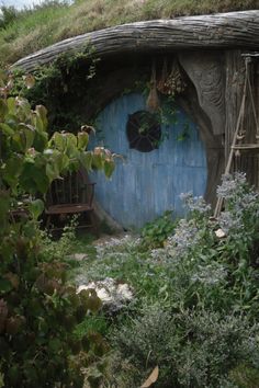 a hobbot with a blue door surrounded by greenery and flowers in the foreground