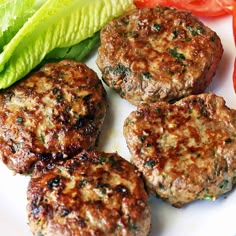 four hamburger patties on a plate with lettuce and tomatoes next to them