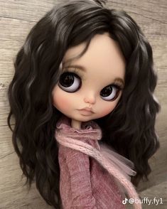 a close up of a doll with black hair and big eyes wearing a pink shirt