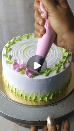 a person is decorating a cake with pink and green icing on the top