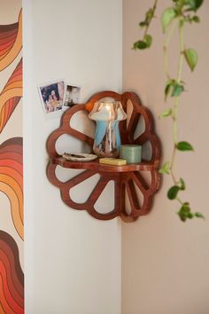 a wooden shelf with pictures on it next to a potted plant and wall hanging