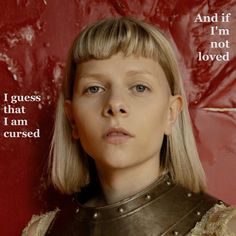 a woman with blonde hair wearing a leather armor and looking at the camera while standing in front of a red wall