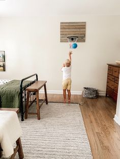 a young boy is playing with a basketball hoop in his bedroom while another child sits on the bed