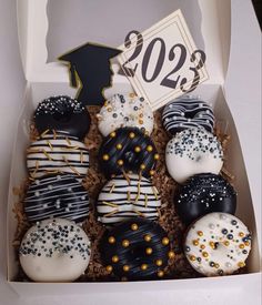 a box filled with lots of decorated donuts next to a graduation hat and sign