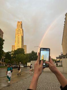 a person taking a photo with their cell phone in front of a building and a rainbow