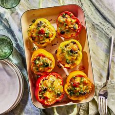 several stuffed bell peppers in a pan on a table with silverware and glasses next to it