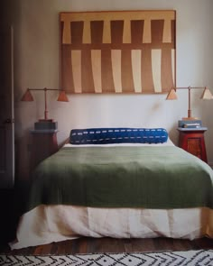 a bed with a green blanket and two lamps on either side of the headboard