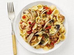 a white bowl filled with pasta and clams on top of a table next to a fork