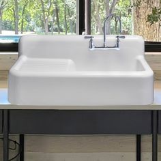 a white kitchen sink sitting on top of a counter next to a window with trees in the background