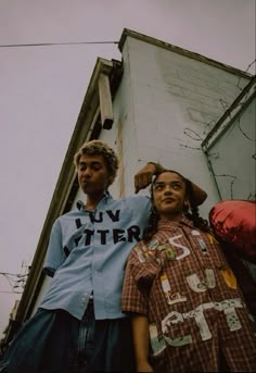 two men standing next to each other in front of a building with graffiti on it