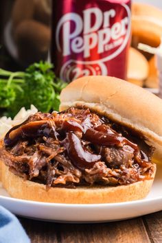 a pulled pork sandwich on a plate with coleslaw and beer next to it