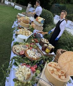 a table full of food and people in the background are standing near some tables that have different types of food on them