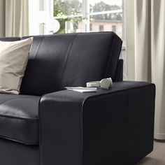 a black couch with two pillows on it in front of a window and a lamp