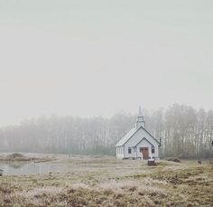 a small white church sitting on top of a grass covered field next to a lake