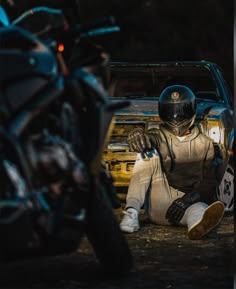 a man sitting on the ground next to a parked motorcycle and another person with a helmet