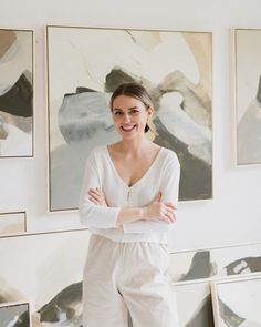 a woman standing in front of some paintings and posing for the camera with her arms crossed