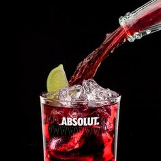 a red drink being poured into a glass with ice and lime wedges in it