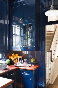 a kitchen with blue cabinets and wooden counter tops in front of an open staircase leading up to the second floor