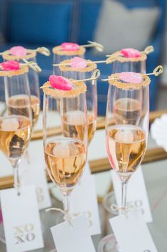 four champagne glasses with pink flowers in them sitting on a table next to each other