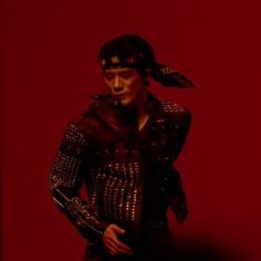 a woman in black and silver outfit with feathers on her head standing against a red background