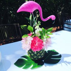 a pink flamingo sitting on top of a pineapple vase filled with flowers and greenery