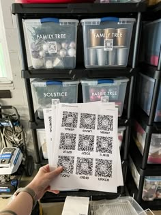 a person holding up some paper with qr code designs on it in front of several storage bins