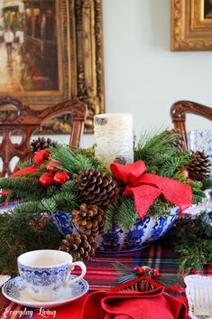 a christmas centerpiece with pine cones, red ribbon and candlesticks on a dining room table