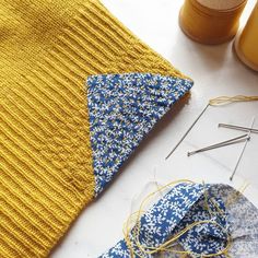 a yellow sweater with blue and white flowers on it next to some knitting needles, yarn and thread