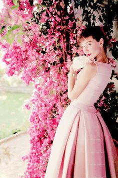 a woman wearing a pink dress standing in front of flowers