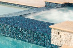 an outdoor swimming pool with blue tile and stone steps leading up to the water's edge