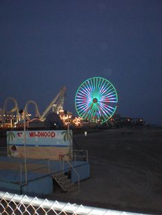 an amusement park at night with ferris wheel in the foreground and carnival rides in the background